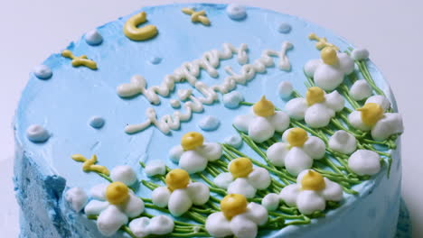 Zooming-in-of-a-close-up-shot-of-a-blue-frosted-birthday-cake,-decorated-with-small-white-flowers-with-yellow-tips-and-green-accents