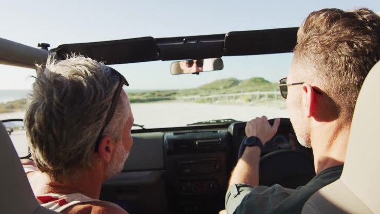 Coppia gay caucasica felice che guida l'auto e parla in una giornata di sole in spiaggia.