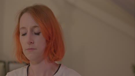 meditating woman with orange hair in bedroom as camera tracks across to her