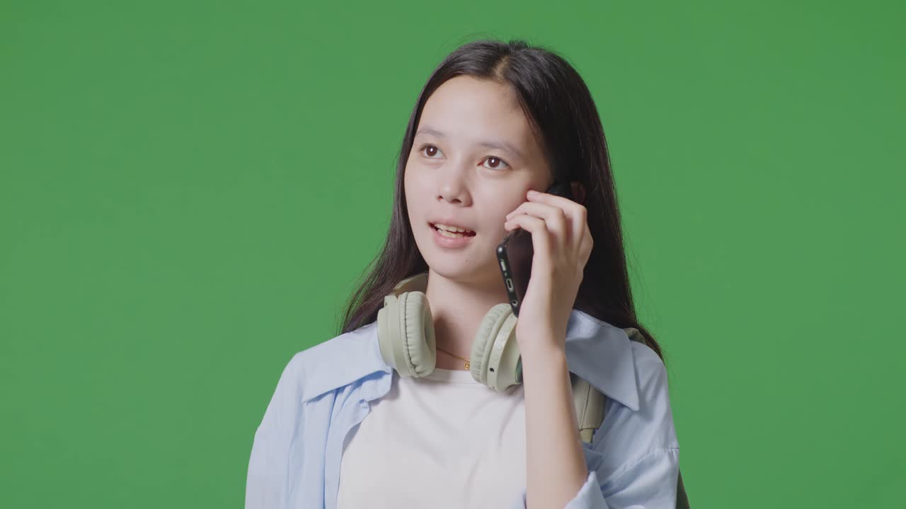 녹색 화면 배경 스튜디오에 서 있는 동안 스마트폰으로 이야기하는 배을 가진 아시아 십대 소녀 학생의 클로즈업