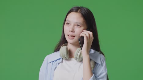 close up of asian teen girl student with a backpack talking on smartphone while standing in the green screen background studio