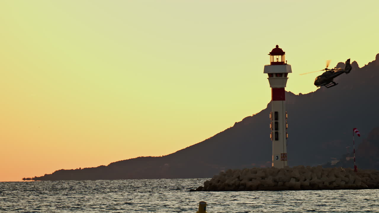 View of a helicopter taking of at sunset near a lighthouse with the mountains on the background in the south of France