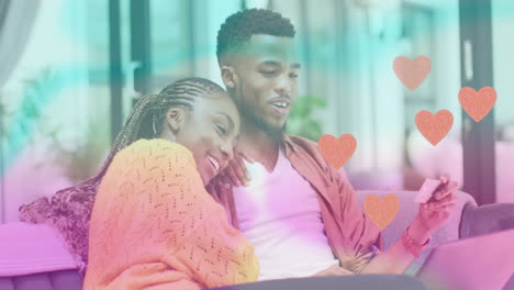 animation of hearts over happy diverse couple using smartphone at home