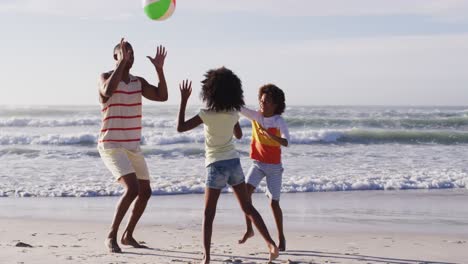 padre afroamericano y sus hijos jugando con una pelota en la playa
