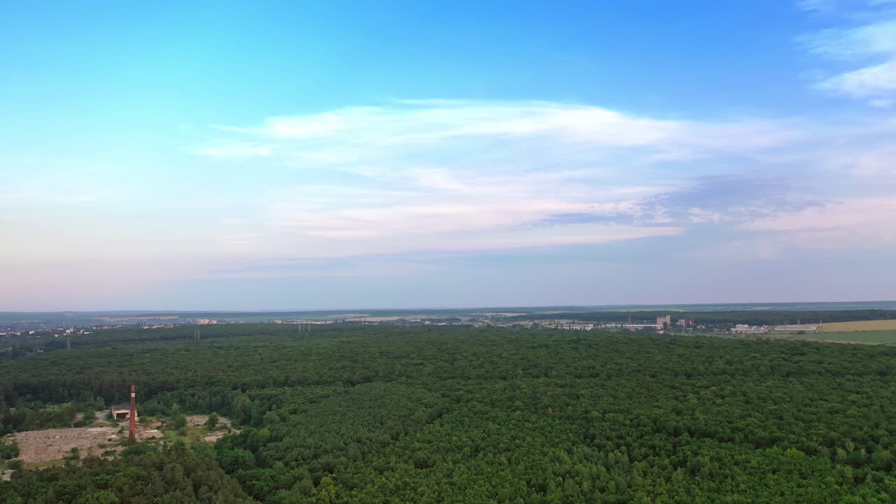 Drone is rising up over the natural environment in summer. Green forest under bright sky outdoors. Beautiful scenery in the countryside.