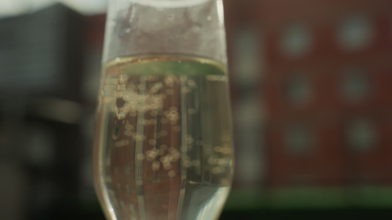 primo piano di un calice di champagne con bollicine su un balcone, bollicine che salgono vivacemente e flussi scintillanti, dettagli di carbonatazione nitidi, sfondo sfocato con skyline di mattoni, atmosfera festosa ed energica, atmosfera da brindisi su un tetto