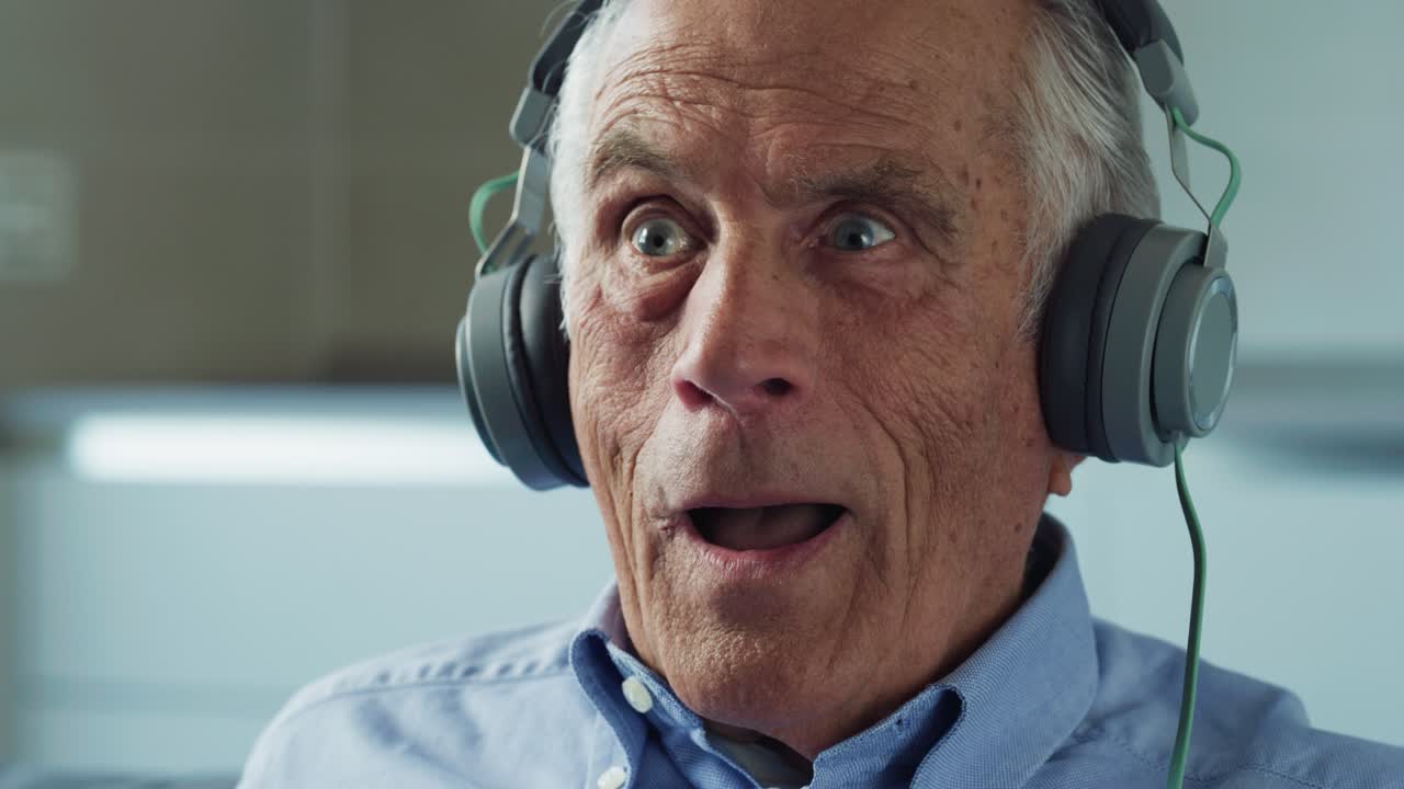 Cinematic close up shot of happy senior pensioner man is having fun to dance and sing while listening to music with headphones at home. Concept of technology, elderly, connection, generation, handicap