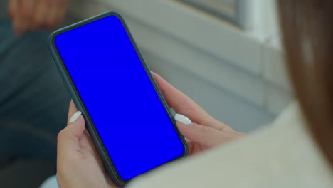 close up of a woman hand holding a mobile telephone with a vertical blue screen in tram chroma key smartphone technology cell phone.