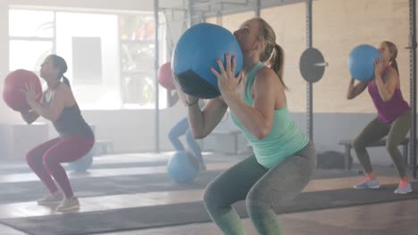 focused unaltered diverse women lifting medicine balls at group fitness class in gym, in slow motion