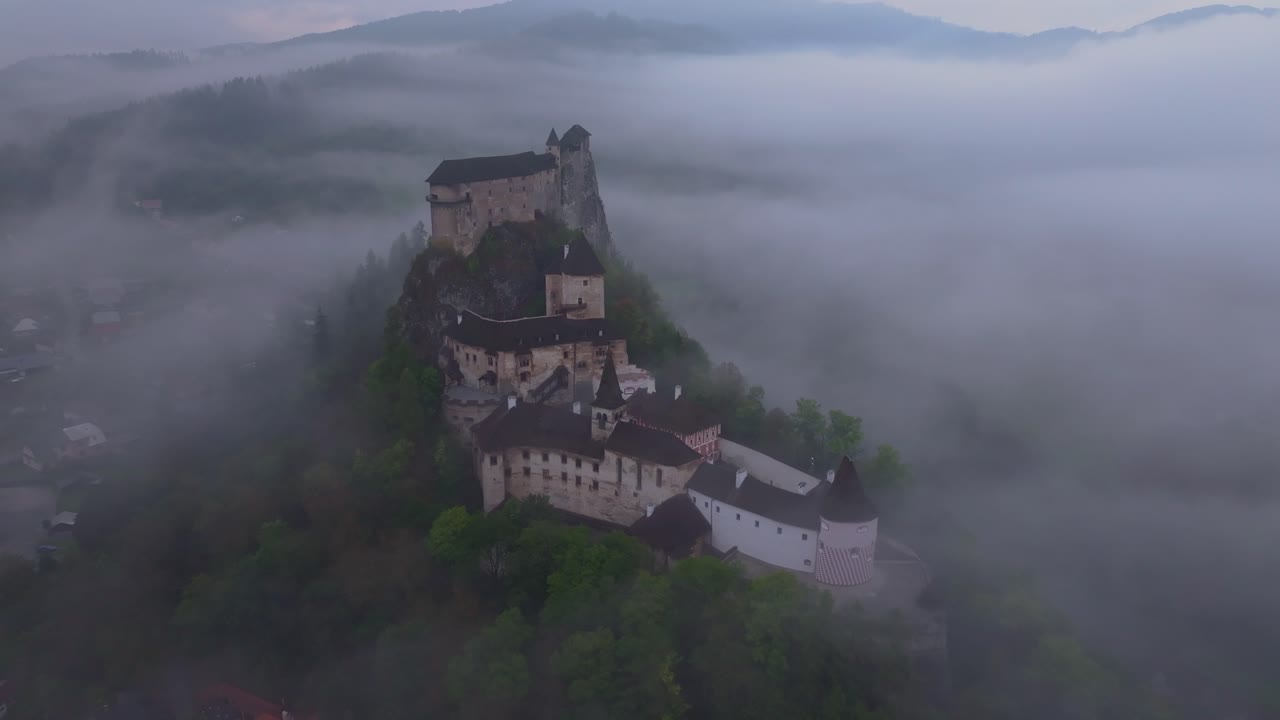 Aerial glimpse of Orava Castle rising above misty valleys at dawn