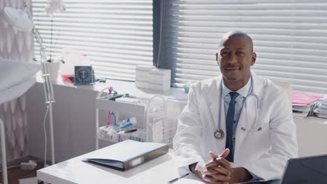 portrait of male doctor wearing white coat with stethoscope sitting at desk in office