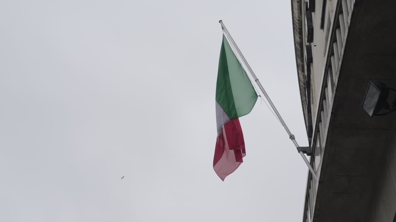 Bandiera nazionale italiana che sventola appesa sulla facciata di un edificio, ripresa al rallentatore.