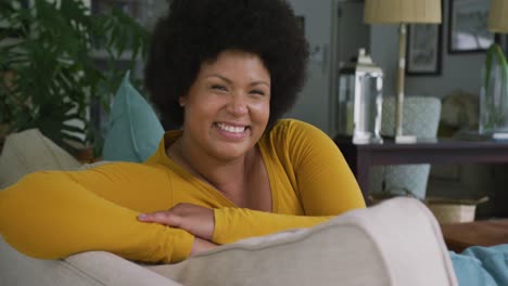 video of happy plus size african american woman sitting on sofa