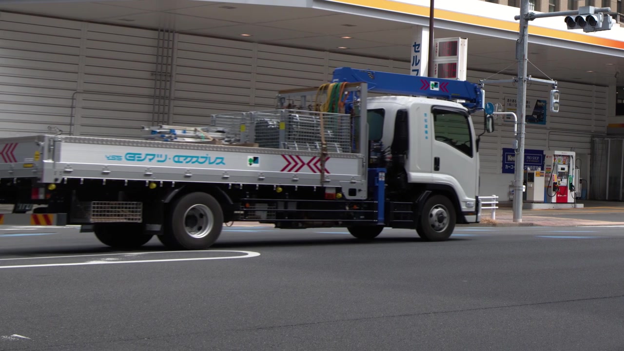 Daytime wide shot of cars and trucks driving through a city intersection in Tokyo, Japan.