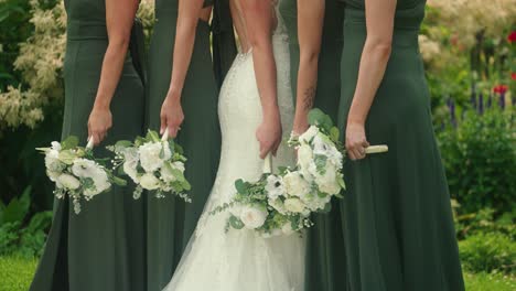 bride and bridesmaids hold bouquets of flowers while posing for a garden photo