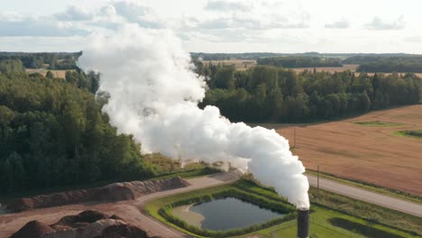 aerial drone shot of a lone factory chimney spewing fumes into atmosphere in rural area