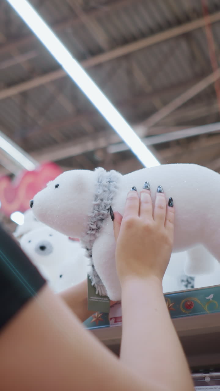 검은 셔츠와 안경을 입은 긴 갈색 머리카락을 가진 웃는 여성의 뒷모습 백색 플러시 북극  장난감과 함께 스카프 상점 선반에 축제 휴가 장식으로 둘러싸여