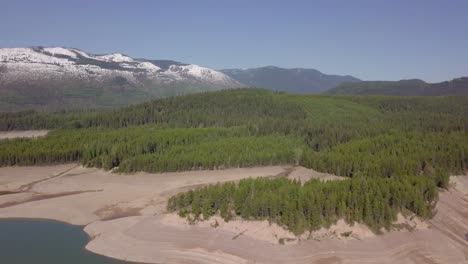 Gran-Bosque-Siempreverde-Al-Lado-De-La-Montaña-Cubierta-De-Nieve-Y-El-Lago-En-Canadá,-Revelación-Aérea