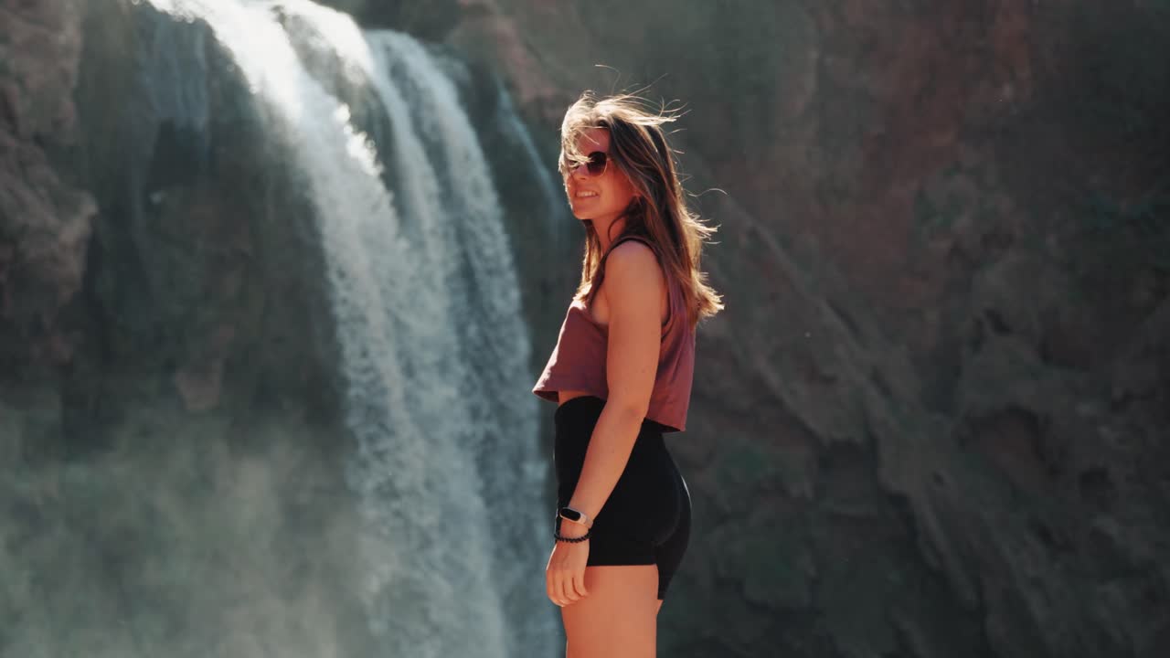Detail of young caucasin woman smiling into camera with sunglasses in front of waterfalls in Ouzoud, Morocco