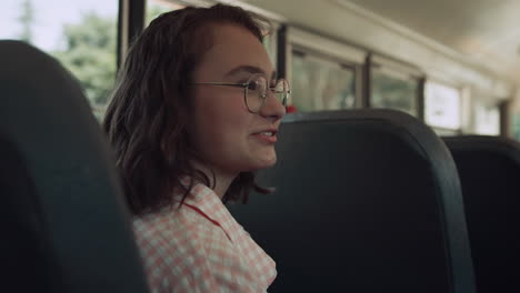 una adolescente sonriente sentada en el autobús de la escuela hablando con sus amigos.