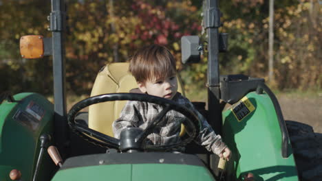 el niño juega con entusiasmo a conductor de tractor. se sienta detrás del volante de un viejo tractor en la granja