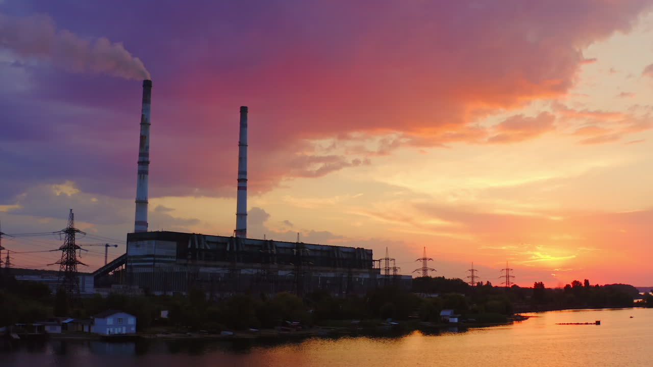 Manufacturing at sunset. Industrial factory near the river on the beautiful colorful background of the sky. Chemical plant with smoke from pipe in the evening.