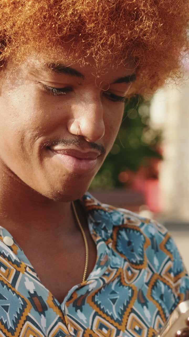 Giovane con capelli ricci arancioni che sorride mentre usa uno smartphone all'aperto