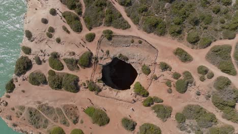 Drone rising above benagil cave, top down bird&#039;s eye view, sandy trails around
