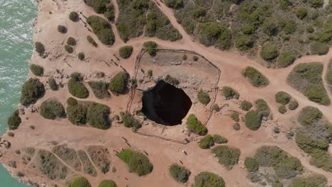 drone rising above benagil cave, top down bird's eye view, sandy trails around