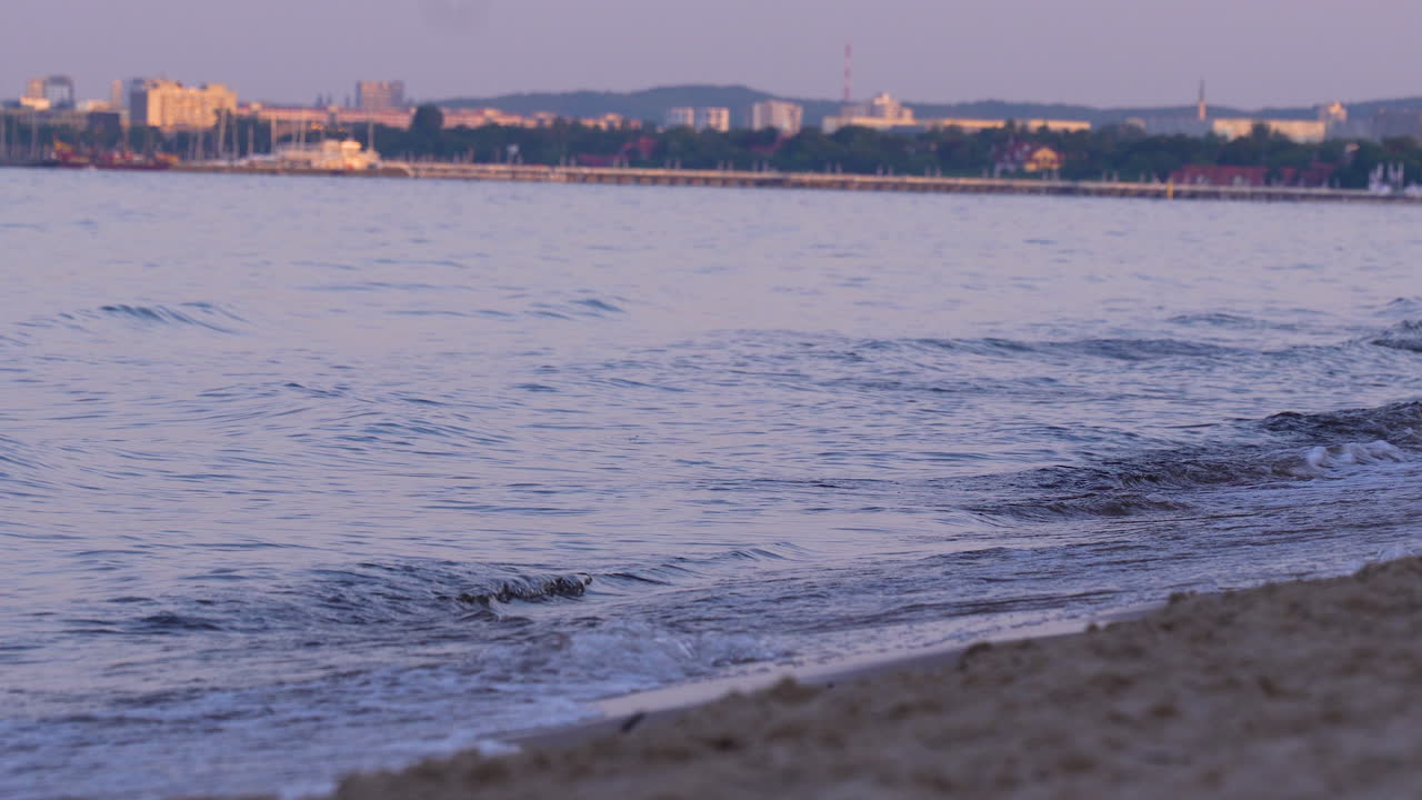 Gentle sea waves reaching sandy coastline with city view