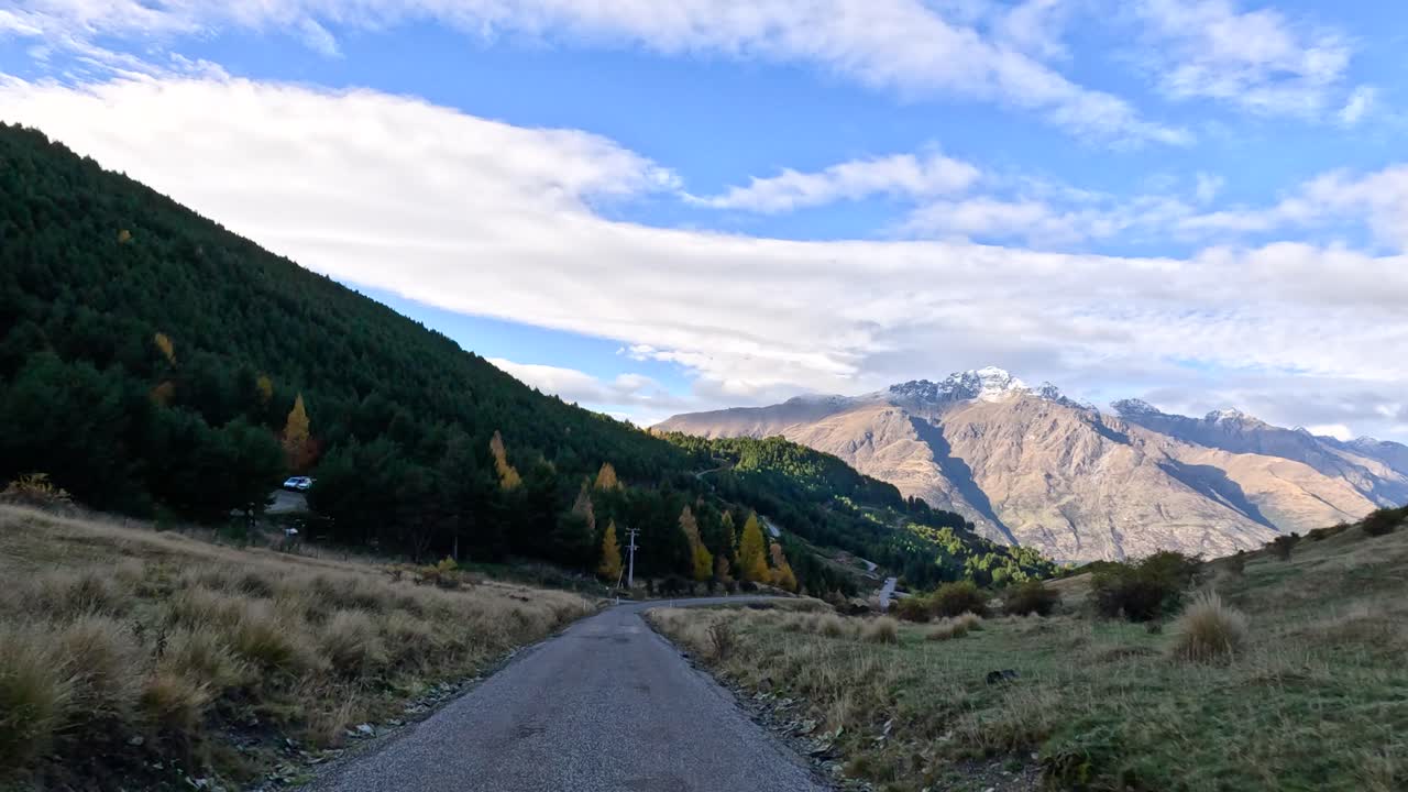 Vehicle travels along winding rural road, lush hills and mountains, daylight, smooth forward camera motion