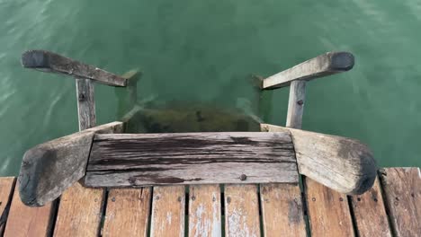 weathered worn wooden ladder descends boardwalk to green ocean water and sandy bottom