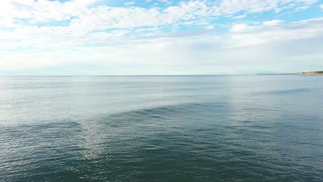 AERIAL:-Locked-Shot-of-Waving-Blue-Calm-Baltic-Sea-with-Cloudy-Sky-and-Horizon-in-the-Background