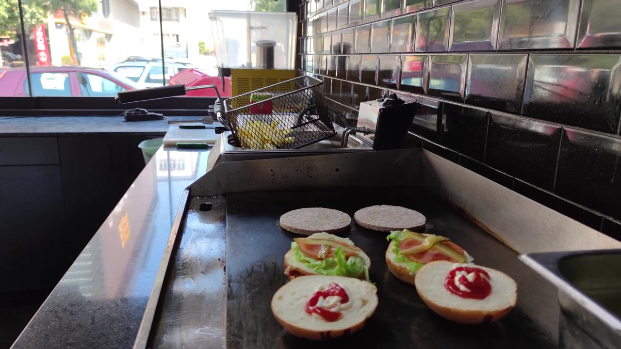Pains à burger et ingrédients cuisant sur une plancha professionnelle.