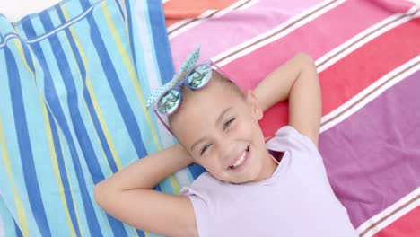 Portrait-of-happy-caucasian-girl-with-sunglasses-lying-on-towels