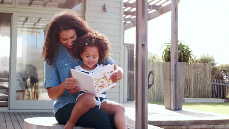 Una-Joven-Negra-Leyendo-Un-Libro-Sentada-En-Las-Rodillas-De-Su-Madre-Al-Aire-Libre