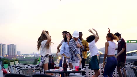 professional dj is working at cool rooftop party with joyful young men and women dancing and having fun enjoying music, leisure and summertime.