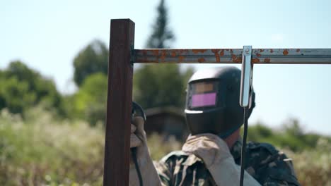 welder in mask fixes parts of future fence against clear sky