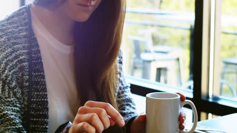 woman having coffee while using on mobile phone