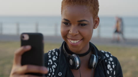 Porträt-Einer-Stilvollen-Afroamerikanischen-Frau,-Die-Ihr-Smartphone-Benutzt-Und-Ein-Selfie-Foto-Macht,-Lächelnd-Posiert-Und-Den-Erfahrungsaustausch-Mit-Mobiler-Kameratechnologie-Am-Meer-Im-Hintergrund-Genießt