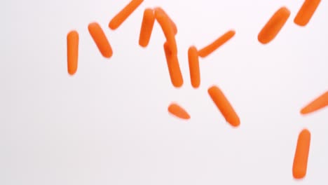 bright orange baby carrots falling on white backdrop in slow motion