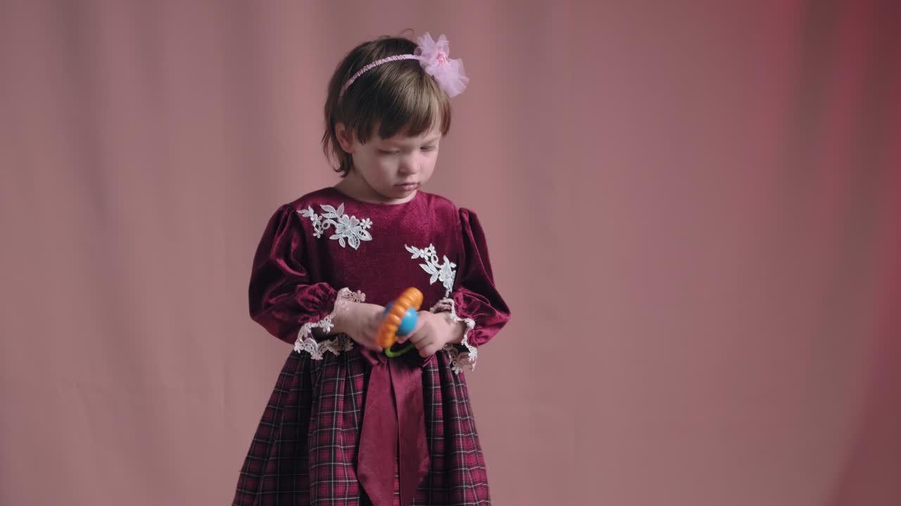 Cute little girl in an vintage burgundy dress is playing with a rattle toy