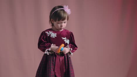 cute little girl in an vintage burgundy dress is playing with a rattle toy