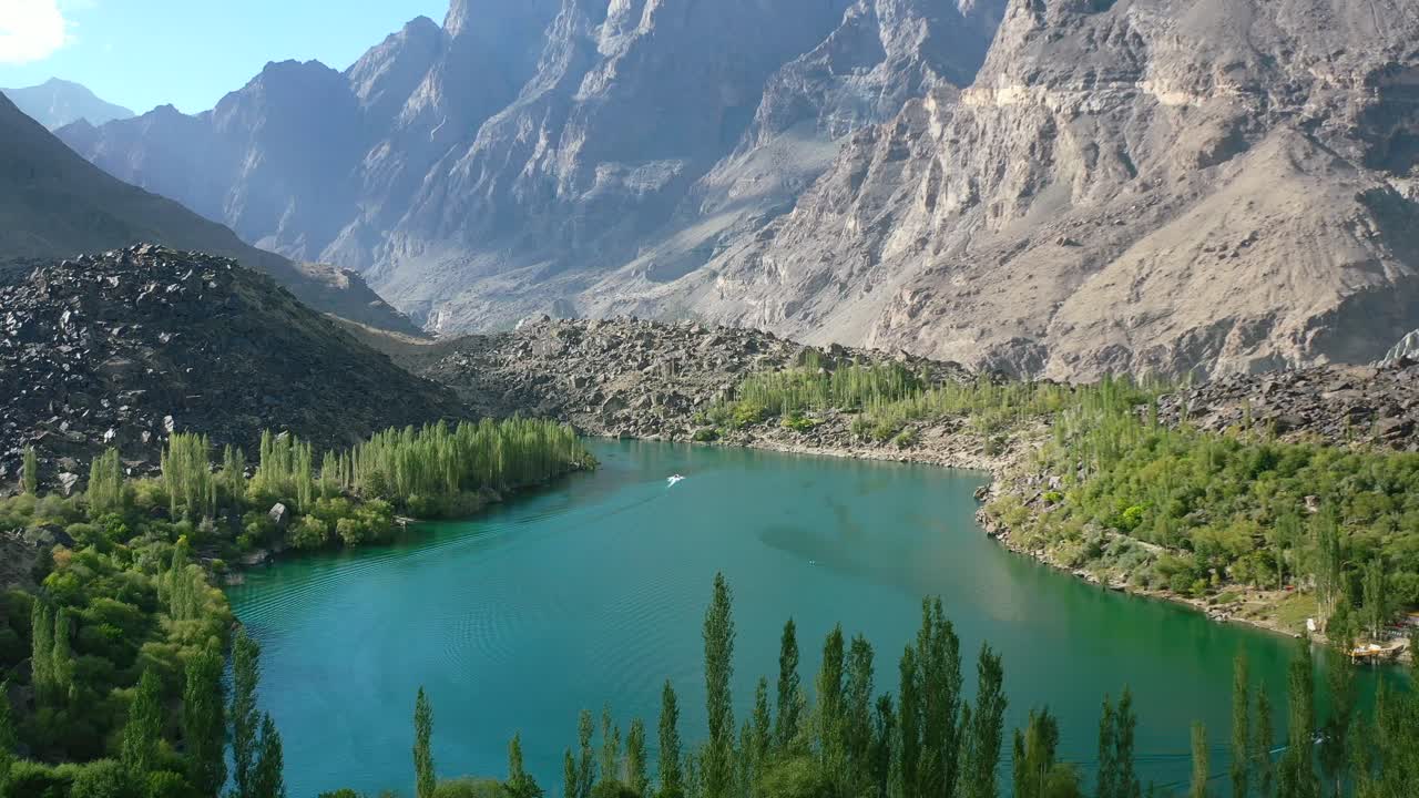 drone aéreo de un barco en el lago kachura superior en skardu pakistán en un día soleado de verano rodeado de bosque verde y una cordillera única en la distancia