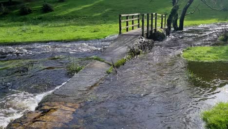 jib shot of rustic stone submerged pathway leading to arched wooden bridge overflowing flooded river