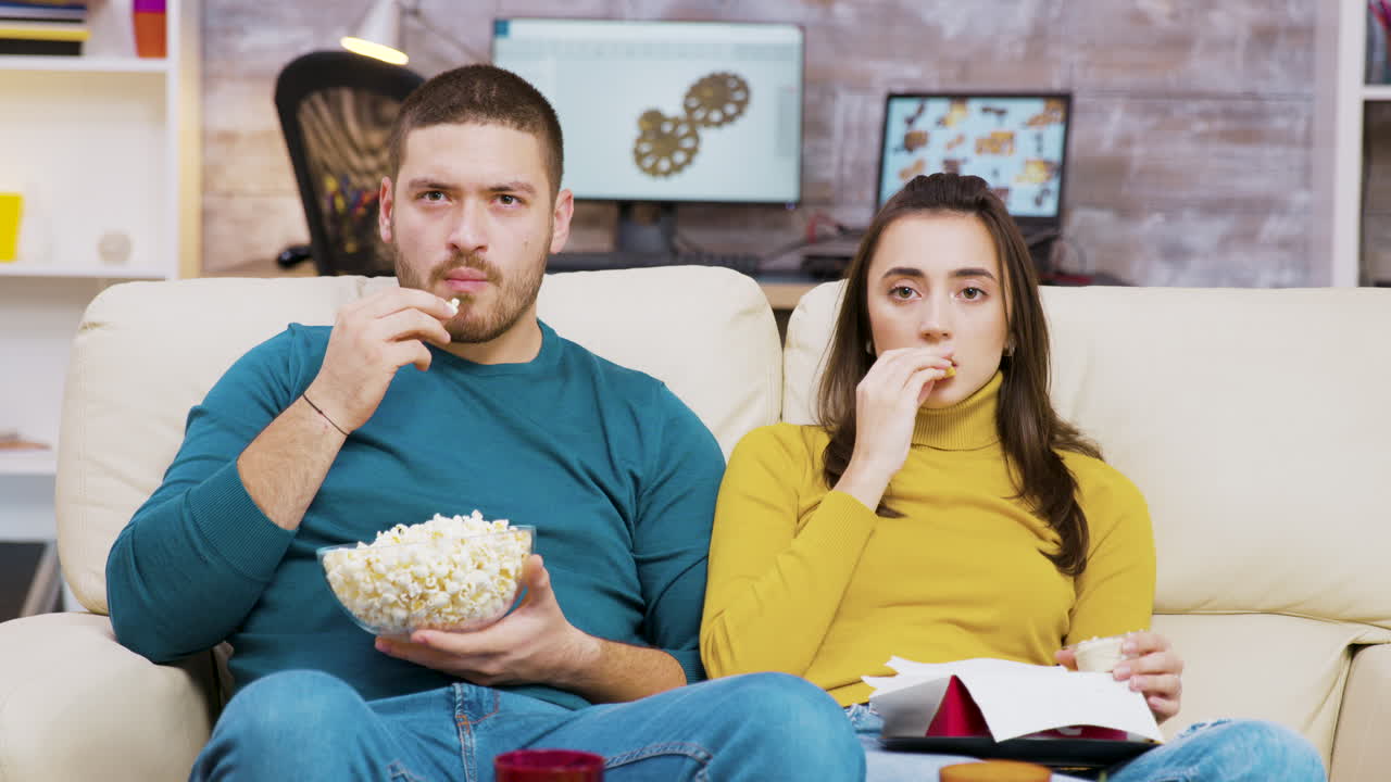пара смотрит телевизор и ест попкорн.