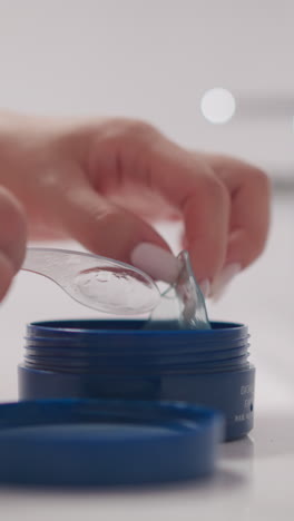 mano de mujer toma parche para la piel de los ojos usando espátula cosmética. dama con manicura toma parches cosméticos para los ojos de la jarra en el baño en cámara lenta
