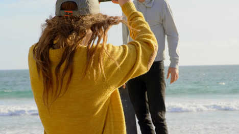 Rückansicht-Einer-Jungen-Kaukasischen-Frau,-Die-Auf-Ein-Foto-Eines-Jungen-Kaukasischen-Mannes-Mit-Kamera-Am-Strand-Klickt-4k