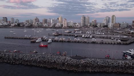 Aerial-view-of-boat-arriving-harbor-of-Punta-del-Este-in-Uruguay-during-dusk---Skyline-buildings-in-background