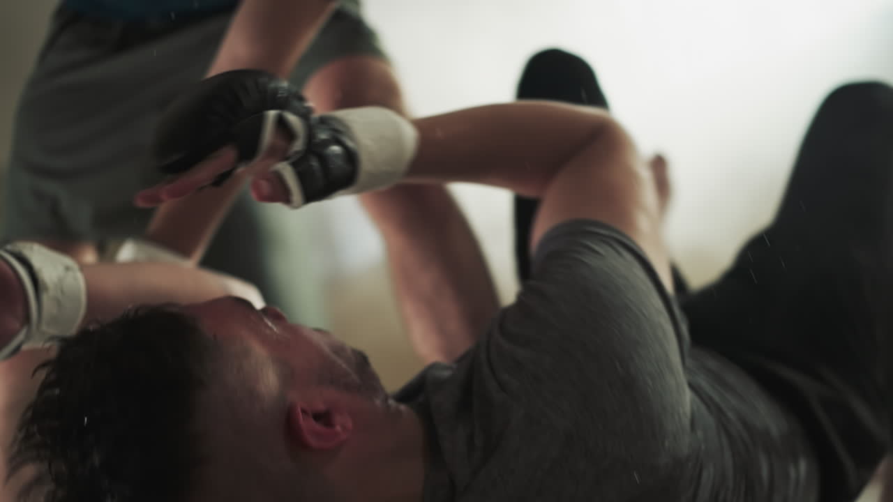 한 남자가 체육관에서 무거운 타격을 놓치고 바닥에 머리를 막습니다. 피곤한 스포츠맨은 무술 클럽에서 스파링하는 동안 손으로 얼굴을 보호합니다.